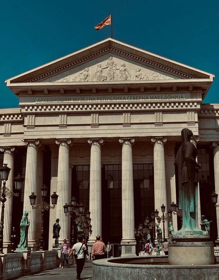 Classical architecture of the Archaeological Museum in Skopje with tourists exploring the site.
