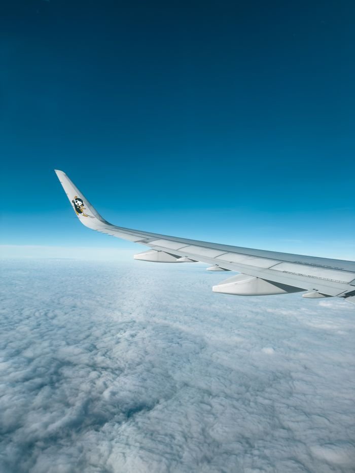 A panoramic view from an airplane, showcasing the wing and a vast sea of clouds below.