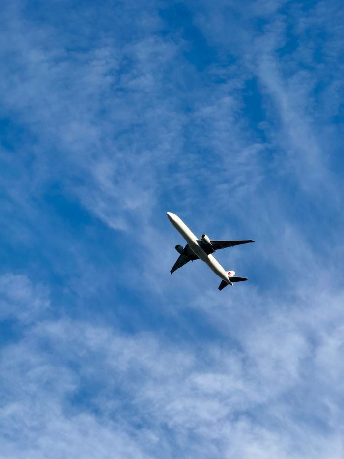 A commercial airplane flying high among wispy clouds in a bright blue sky.